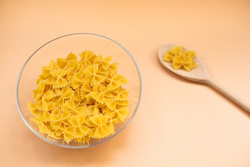 Butterfly pasta in glass bowl and wooden spoon on beige background