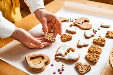 Woman decorating heart shaped cookies with frosting. Glazed festive homemade biscuits in form of hearts.
