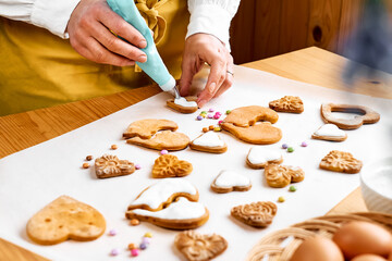 Woman decorating heart shaped cookies with frosting. Glazed festive homemade biscuits in form of hearts.