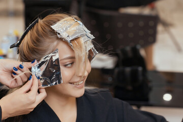 Hair stylist makes bouffant using comb on thin strands. Shatush technique for hair lightening.