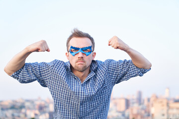 Pumped fists or superpower, aggression emotion concept. Caucasian man in nightwear shirt and superhero blue mask showing strength gesture and angry face. High quality image