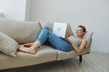 Teenage girl freelancer with laptop sitting on couch at home smiling in home clothes and glasses with short haircut, lifestyle with no filters, free copy space