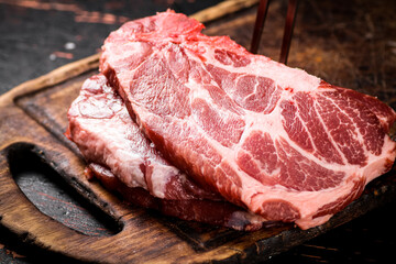 Raw pork steak on a cutting board with fork. 