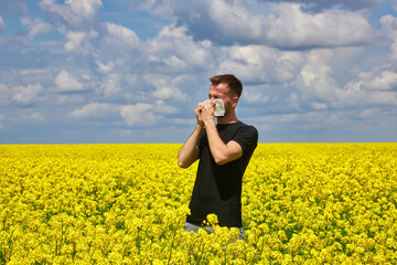 man in yellow canola field blowing his nose and suffering from pollen allergy.