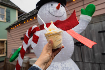 Hand holds a cup of soft serve ice cream, with a snowman Christmas decoration in the background