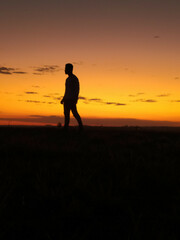 young man walking emotionless looking left silhouetted in sunset with orange sky in background