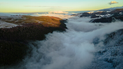 Landscape photography of mountains with clouds in a valley shot from a drone at sunset in the winter season. Aerial photography of mountains at sunset