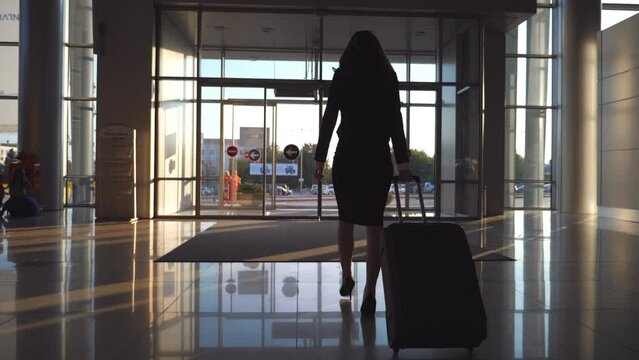 Young woman in heels walking with her suitcase along airport hall or waiting room. Follow to business lady going to exit from terminal with her luggage. Trip or vacation travel concept. Slow motion