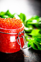 A full jar of red caviar with parsley on the table.