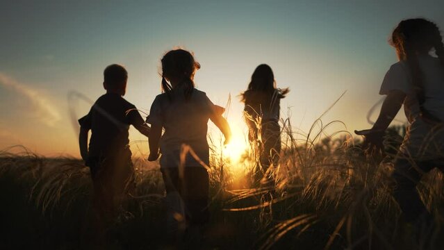 Active happy family. Group of kid run together across field at sunset.Team of kid active games in nature.Silhouette of happy children outdoors in park.Kid child run on green grass.Children family play