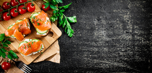 Salmon sandwich on a cutting board with herbs and tomatoes. 