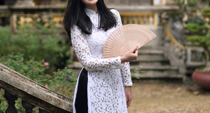 Vietnamese woman in traditional dress Ao Dai, holding a wooden fan