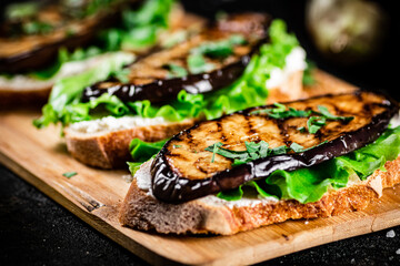 Sandwich with grilled eggplant and lettuce on a wooden cutting board. 