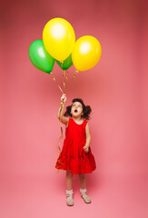 Fototapeta na wymiar Portrait of a cheerful little girl isolated on a pink background, holding a bunch of colorful balloons, posing.