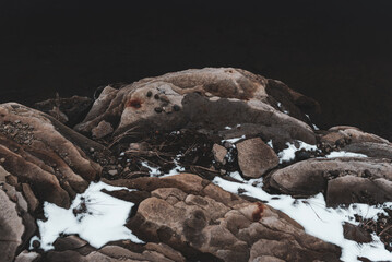 Outcrop of rock on the shore with snow and traces of rust from stones.