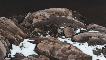 Photo of a rock outcrop on the shore with dark water with snow.