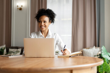 Student online training is a contented young curly-haired woman using a computer, sitting at a workplace at home. Courses in online education via a social network.