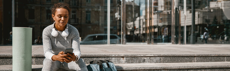 Obraz premium Focused healthy woman texting after having intensive training outdoors. Active lifestyle, sport