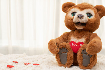 Valentine's day concept. A cute brown teddy bear with big eyes sits on a rug against a window with a bright red heart.