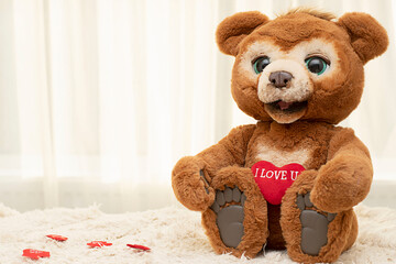 Valentine's day concept. A cute brown teddy bear with big eyes sits on a rug against a window with a bright red heart.