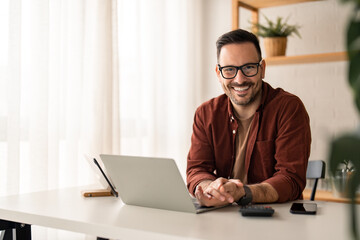 Smiling confident businessman looking at camera sitting at home office desk. Modern stylish corporate leader, successful CEO executive manager wearing glasses posing for business portrait.