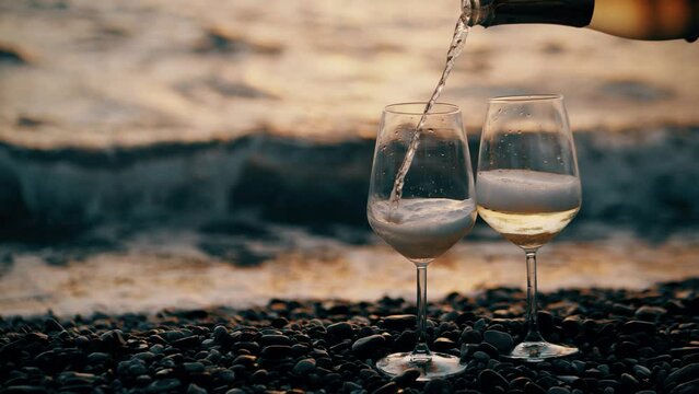 Pouring sparkling white wine into glass on pebble beach