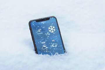 Phone with the current temperature in Celsius and with the weather forecast for the coming days. Modern app interface. The phone sank into the snow