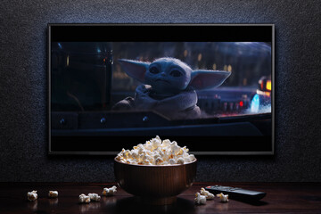 Naklejka premium TV screen playing Mandalorian trailer or movie. TV with remote control and popcorn bowl. Moscow, Russia - January 18, 2023.