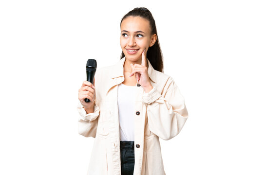 Young singer woman picking up a microphone over isolated chroma key background thinking an idea while looking up