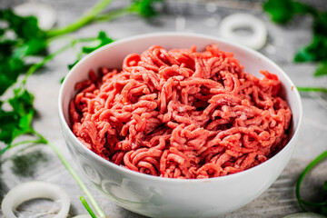 Minced meat in a bowl on a table with parsley and onion rings. 