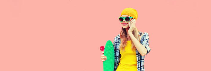 Portrait of happy smiling young woman calling on smartphone with skateboard looking away wearing...