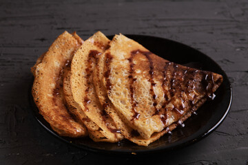 photo three pancakes in the form of a triangle on a plate poured with chocolate syrup
