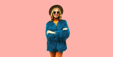 Fashionable portrait of stylish young woman, female model posing wearing blue faux fur, round hat on pink background