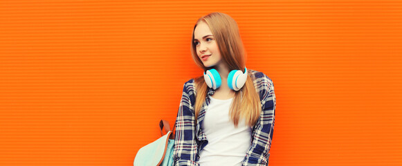 Portrait of happy young woman in headphones listening to music on colorful orange background