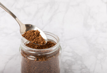 Instant coffee in a spoon and a glass jar on a white marble background. Place for text. Space for copy text