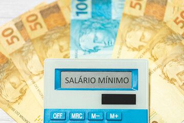 A palavra salário mínimo em Português do Brasil escrita no visor de uma calculadora com notas do...