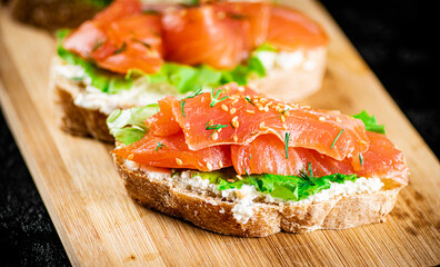 Sandwich with pieces of salmon on a cutting board. 