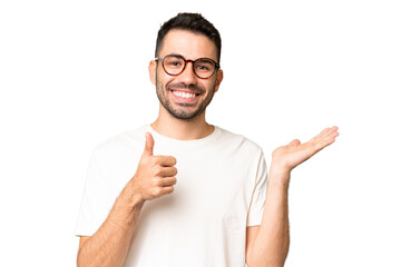 Young handsome caucasian man over isolated chroma key background holding copyspace imaginary on the palm to insert an ad and with thumbs up - Powered by Adobe