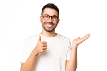 Young handsome caucasian man over isolated chroma key background holding copyspace imaginary on the palm to insert an ad and with thumbs up