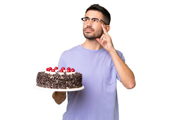 Young caucasian man holding birthday cake isolated on green chrome background having doubts and...