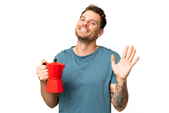 Brazilian man holding coffee pot over isolated chroma key background saluting with hand with happy expression
