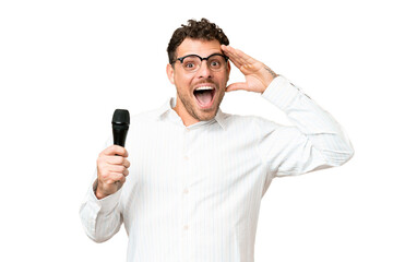 Brazilian man picking up a microphone over isolated chroma key background with surprise expression