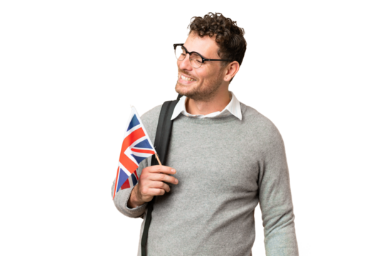 Brazilian man holding an United Kingdom flag over isolated chroma key background looking to the side and smiling