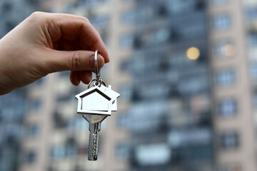 House key in female hand on background of new residential buildings. Real estate agent, moving home...
