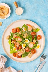 Caesar salad with romaine lettuce, cherry tomatoes, boiled quail eggs and croutons on a light ceramic plate on a blue concrete background. American cuisine.
