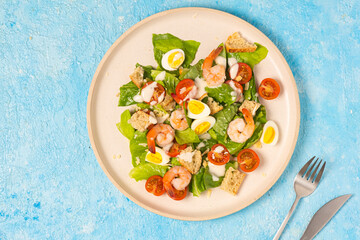 Caesar salad with romaine lettuce, cherry tomatoes, boiled quail eggs and croutons on a light ceramic plate on a blue concrete background. American cuisine.