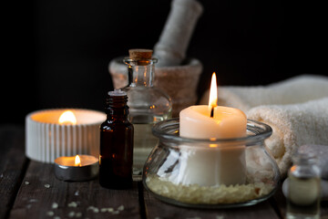 Spa setting with essential oil, candle, sea salt, pebbles, towel on dark wooden background. Massage, aromatherapy. Natural organic ingredients for relaxation, detention. Wellness in salon concept