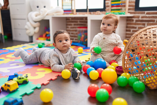 Two adorable babies playing with balls sitting on floor at kindergarten