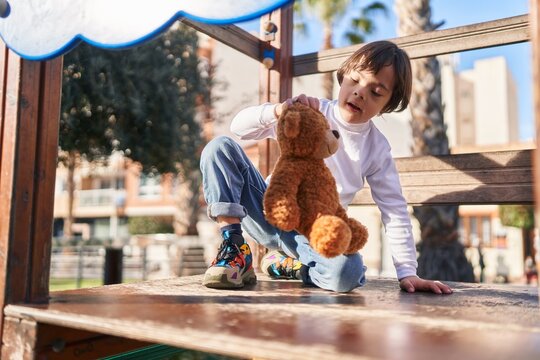 Down syndrome kid playing with teddy bear on slide at park