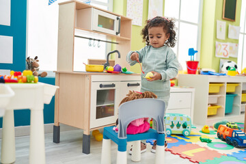 Adorable hispanic girl playing with play kitchen standing at kindergarten